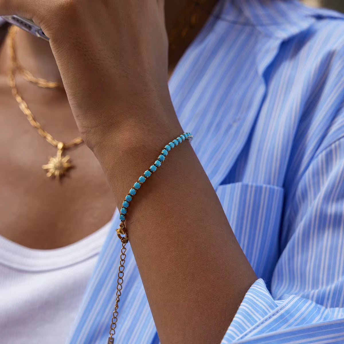 Close-up of a person wearing a turquoise beaded bracelet and gold necklace.