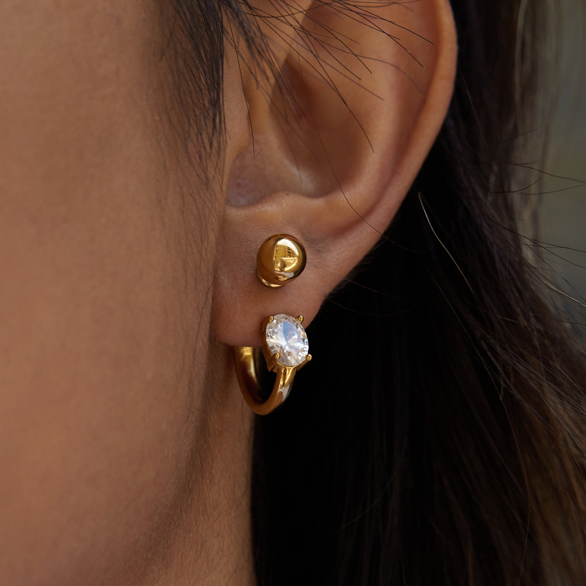 Close-up of an ear wearing Soleil Hoop Earrings with a central oval zircon gemstone.