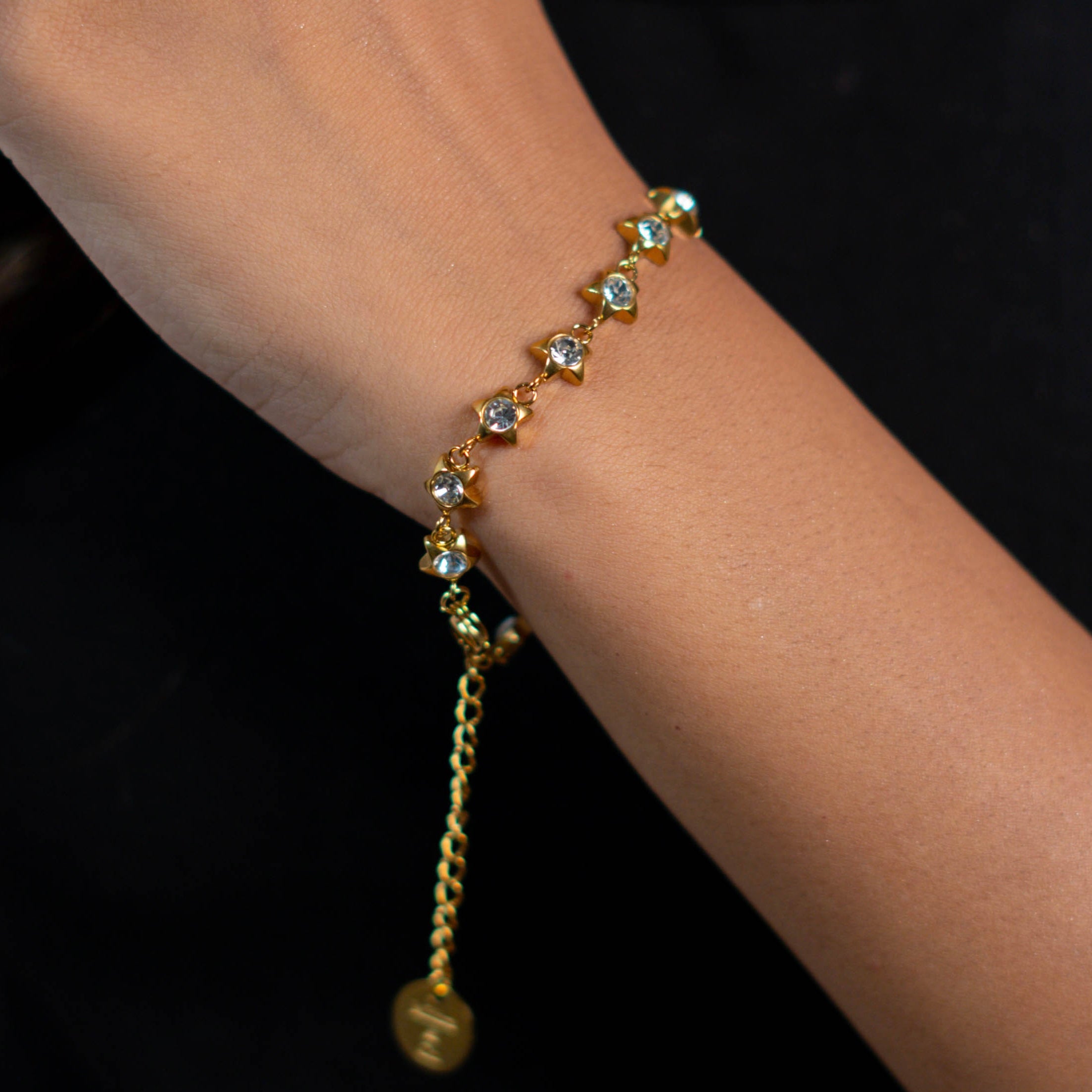 Gold plated maya bracelet with star-shaped charms on a wrist against a dark background