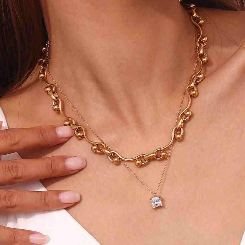 Woman wearing 18k Gold Plated wavy beaded necklace layered with a delicate silver chain necklace with a square pendant