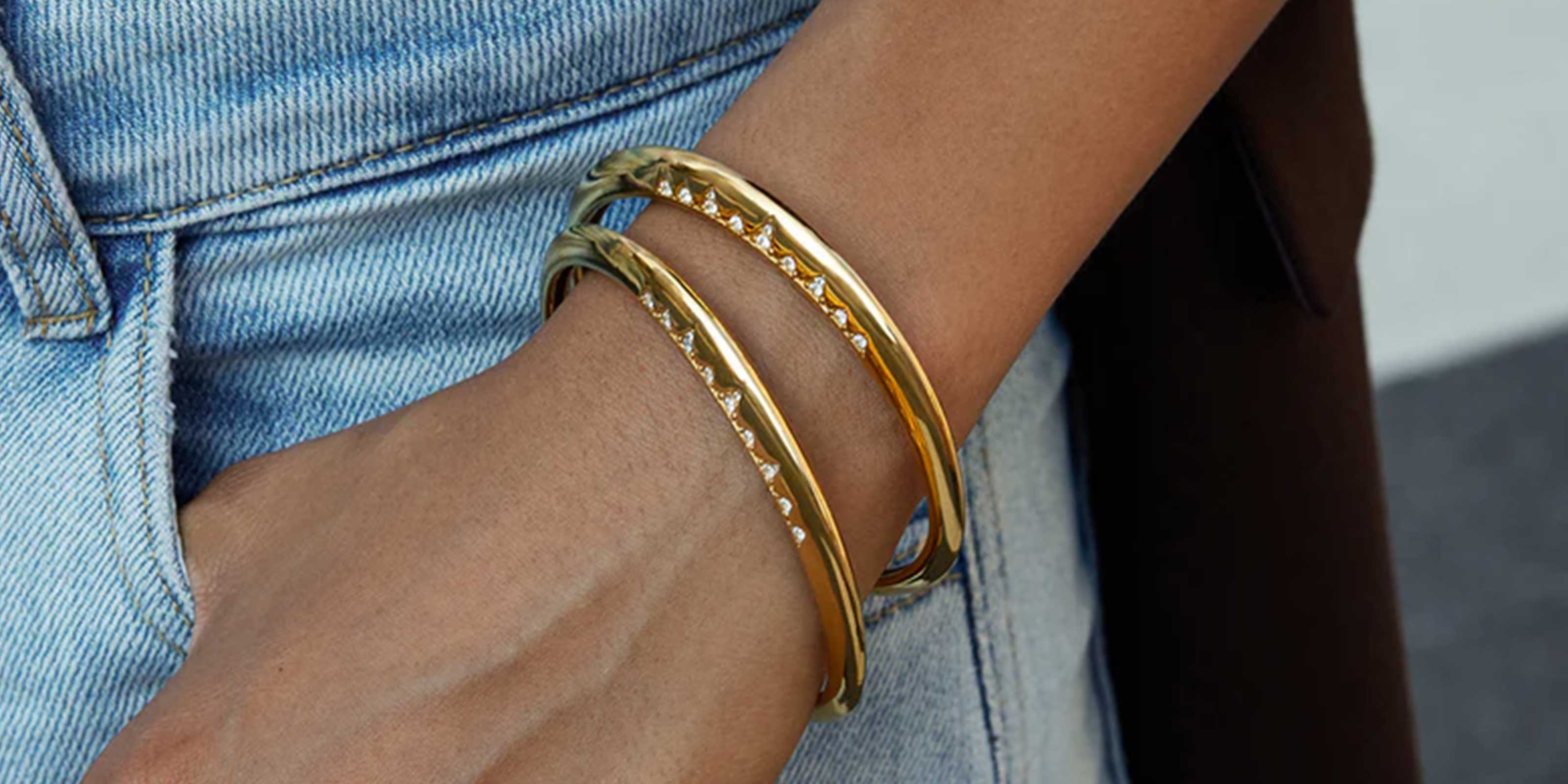 Bangles Cuffs Collection Showcasing Girl Wearing Gold bangles and bracelets on a wrist with thumb in pocket of blue jeans.