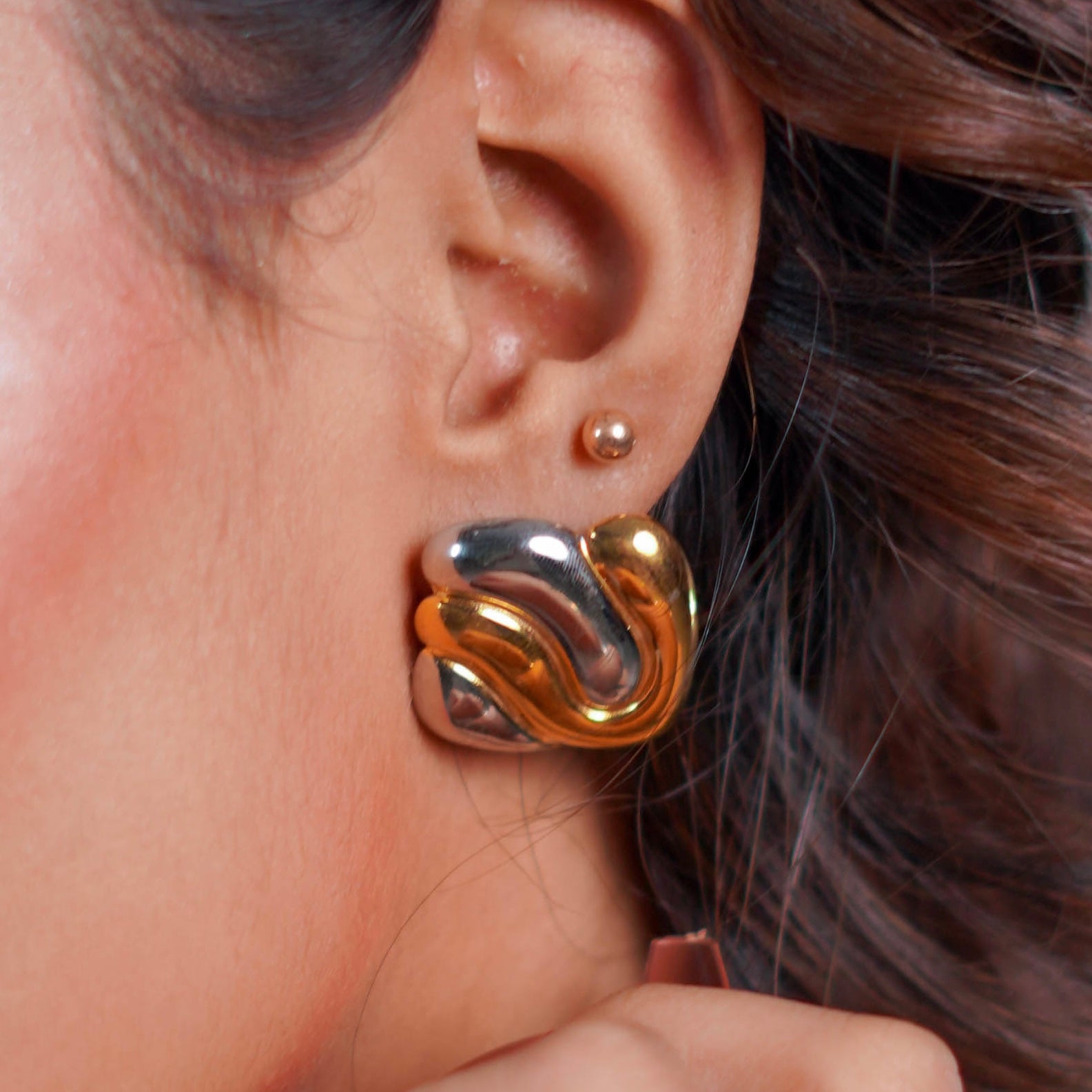 Gold and silver square knot design metal interlock studs worn by a person with brown hair.