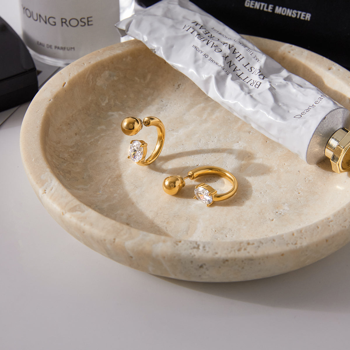 Soleil G-Shape Gold Hoop Huggie Earrings on a stone dish with a product packaging in the background