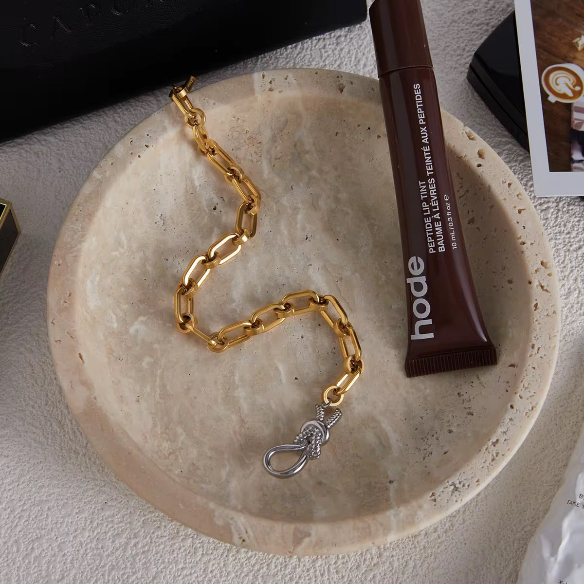 Gold chain necklace on a stone surface with a tube of hode product.