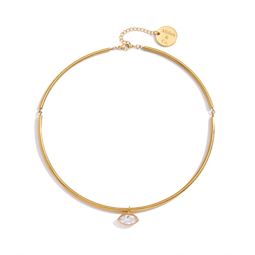 A delicate gold bangle necklace with a small clear marquise-cut gemstone pendant and an adjustable chain with a circular gold tag engraved with 'Mikala Co.' on a clean white background.