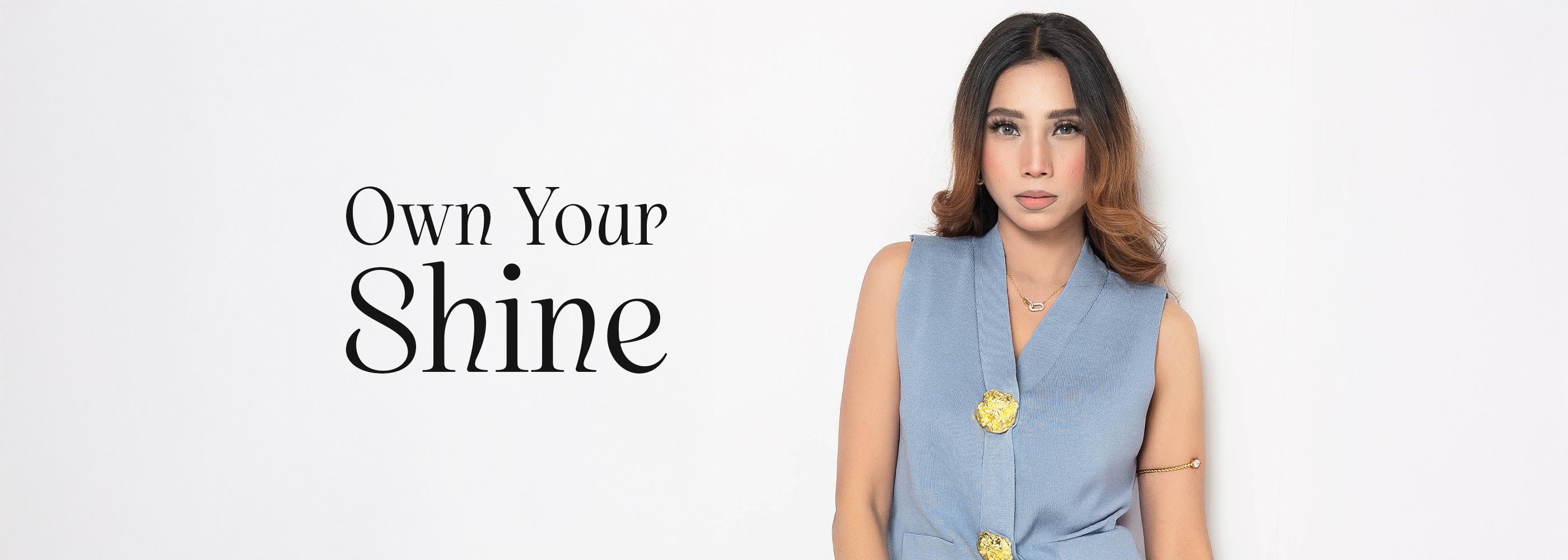Woman wearing artificial jewelry and a light blue sleeveless top with text 'Own Your Shine' on a white background