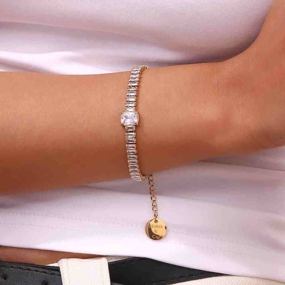 Closeup of hand wearing Alexa Tennis Bracelet with Diamond-cut and baguette crystals with a solitaire station and Mithra & Co. Engraved Tag.