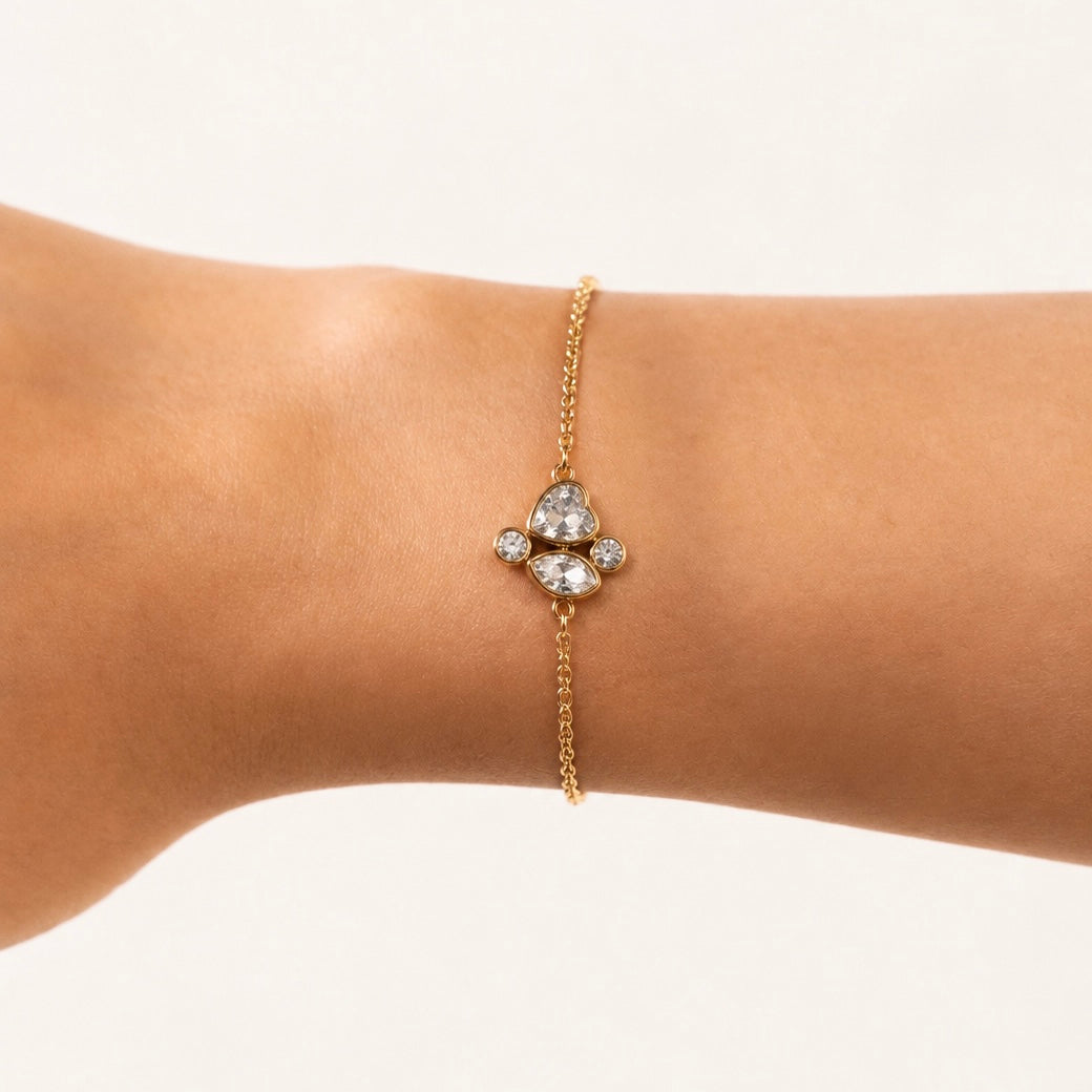 A delicate gold plated Cluster Charm chain bracelet with a central cluster of clear gemstones, shown worn on a person's wrist against a plain light background.