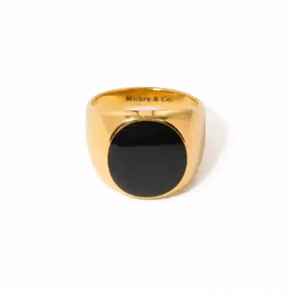 A chunky gold plated Ramsey signet ring with a circular black onyx, with the brand name 'MITHRA & CO.' inscribed on the gold band.