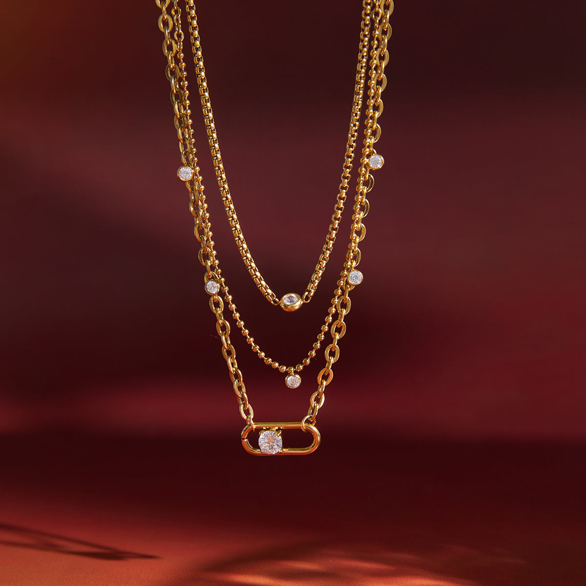 Gold plated 3 layer chain necklace with small diamonds on a red background