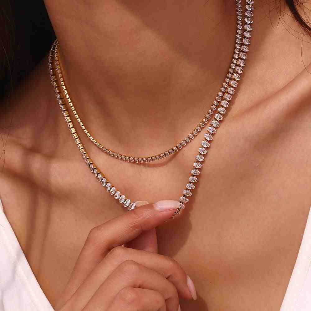 Close-up of a woman wearing the Diamond Cut Neckchain layered with the Linea Necklace, with a hand holding the sparkling 8A zircon station choker.