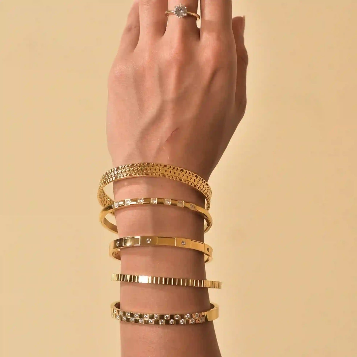 Closeup of a woman's hand wearing claro cuff, bentley cuff, nola bangle with 2 other gold plated bangles and single stone ring.