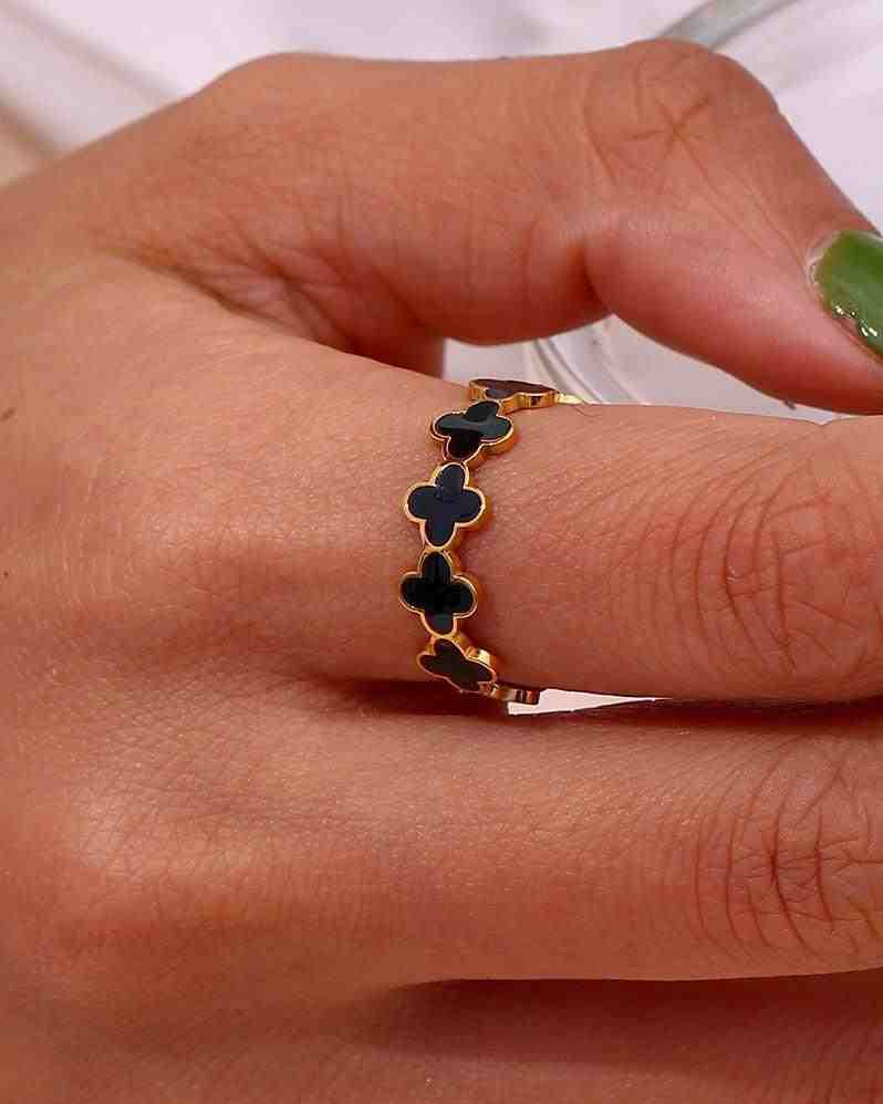 Closeup of a woman's hand wearing 18k gold plated clover back band ring with adjustable enamel four-leaf clover motif design.