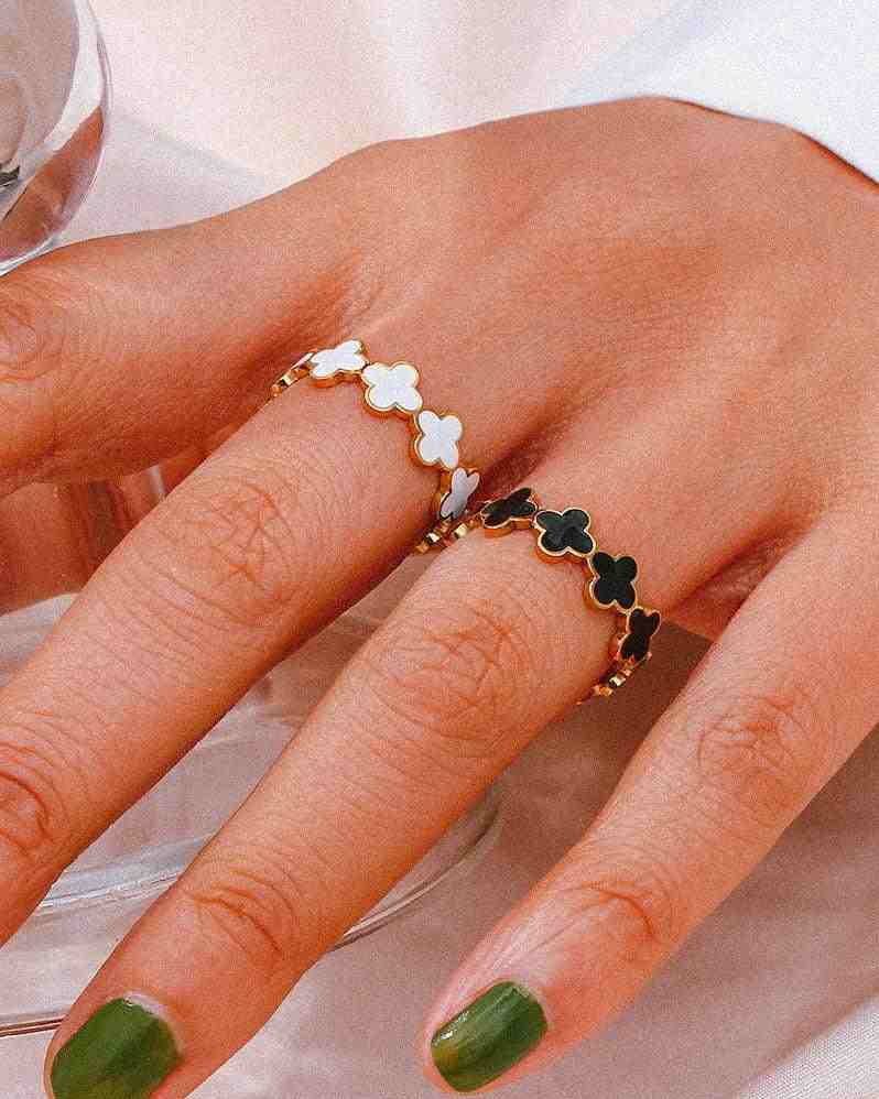Closeup of a hand wearing Waterproof 18k Gold plated Clover Black Band at and clover white band rings with adjustable enamel four leaf clover motifs.