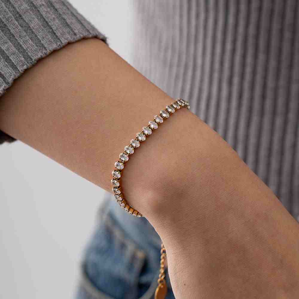 closeup of girl hand wearing gold plated tennis style linea bracelet with diamond cut cut Zircons on a grey shirt.