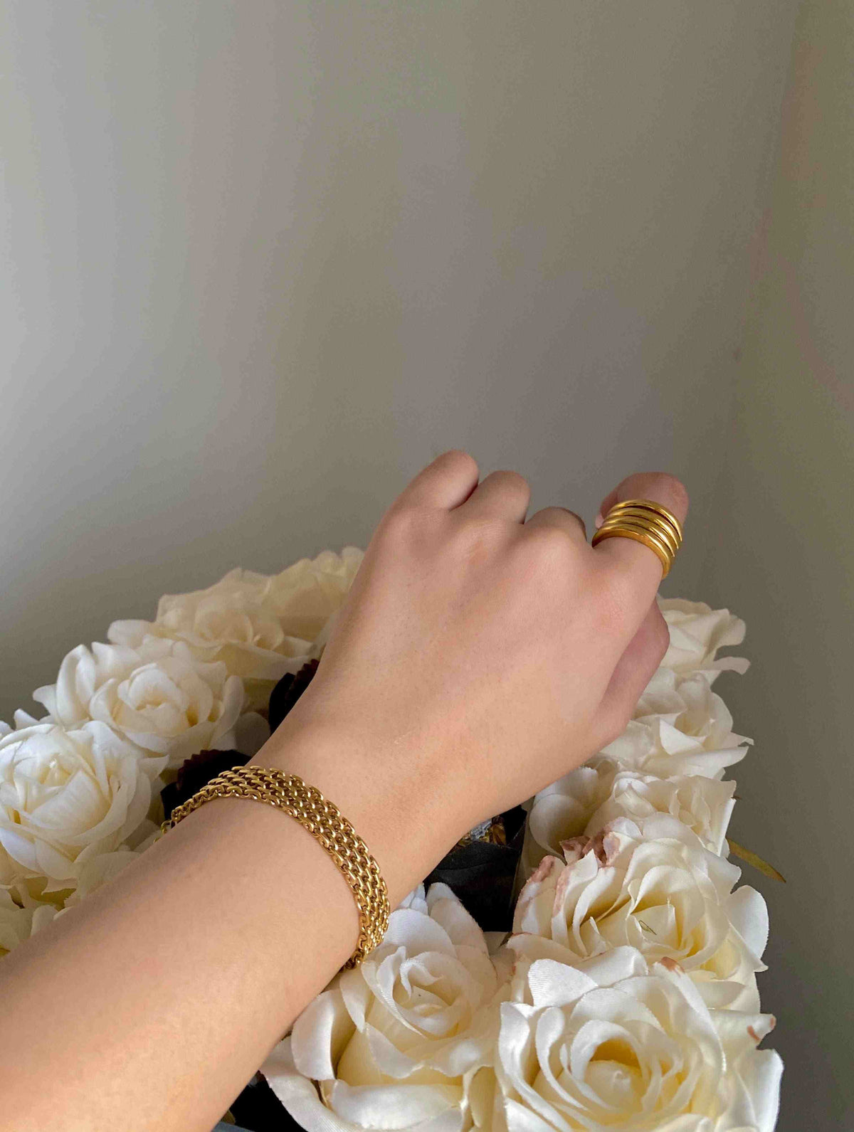 Wrist wearing 18k gold plated mesh style Rowena bracelet, set against a soft background of white flowers.