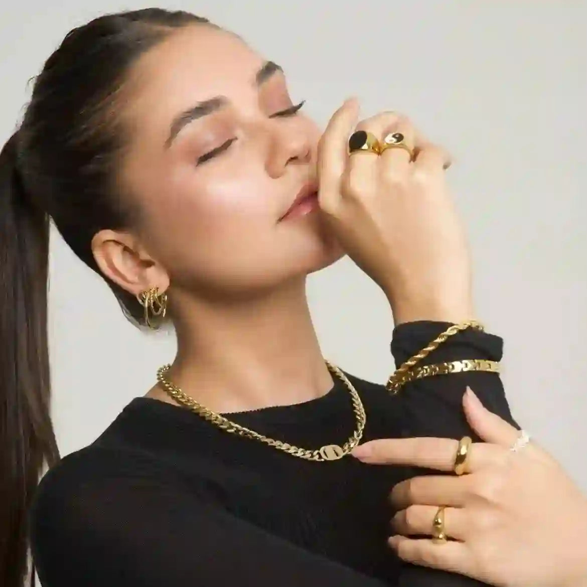 Girl wearing 5 gold rings including ramsey signet, necklace, and earrings, posing with hands styled to show all jewelry.
