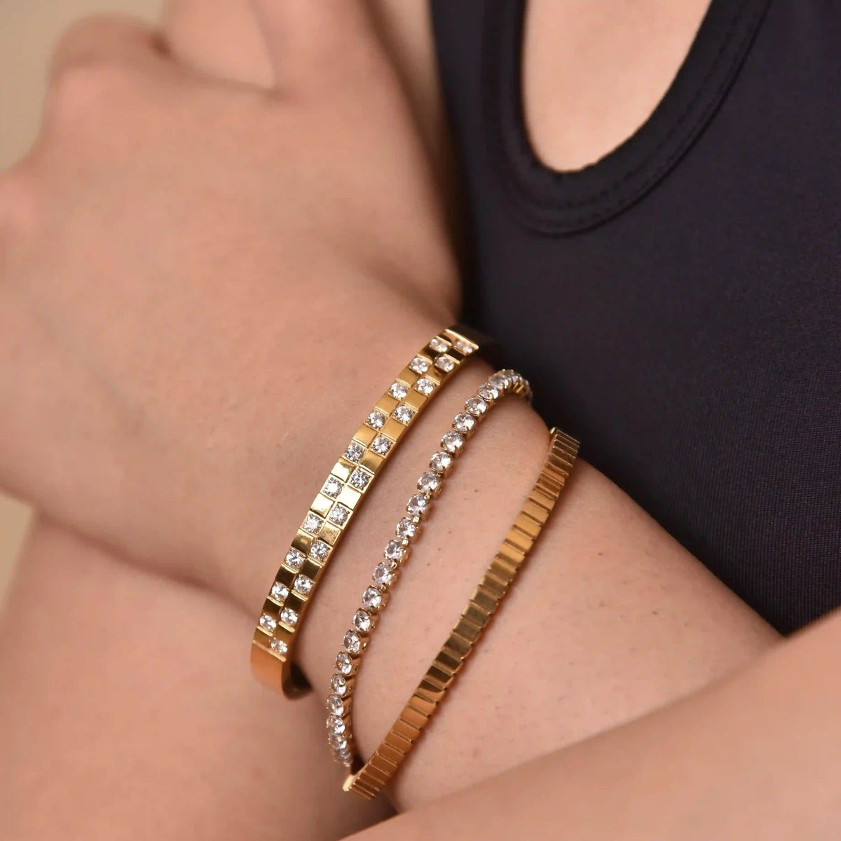 cloesup of woman hand wearing 18k Gold Plated verity basic tennis bracele and brillante cuff and bentley cuff stacked all toether.
