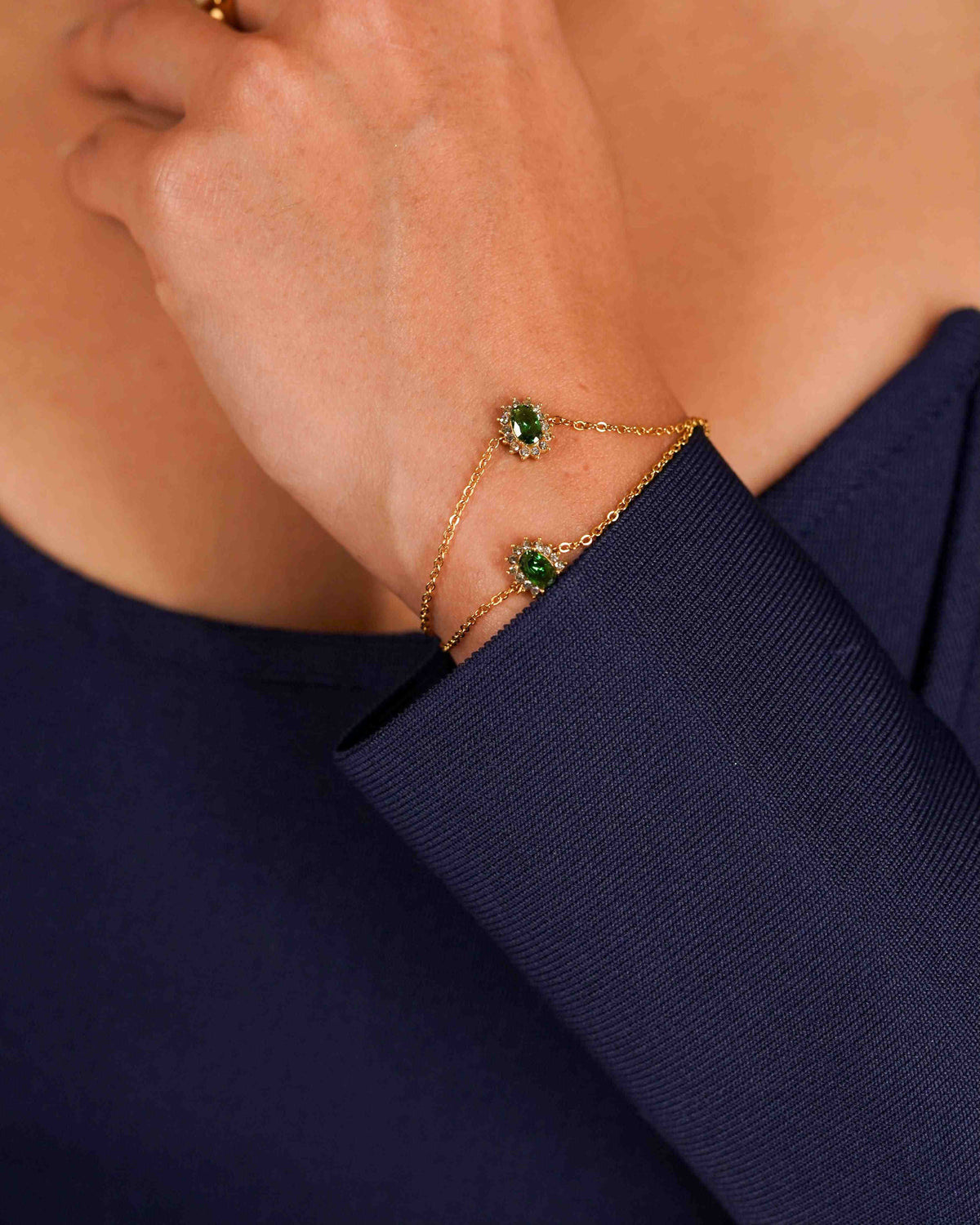 closeup of a woman's wrist wearing Prasino bracelet with oval green center gemstone with pave halo of micro zircons against a navy background.