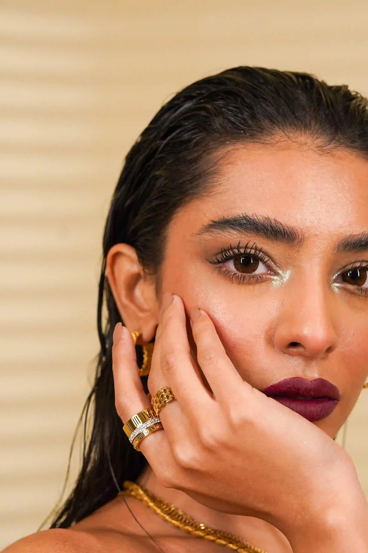 Close-up of a woman wearing Trilogy Stack Ring gold plated with Roman Numerals, mesh ring, a gold plated earring and necklace.