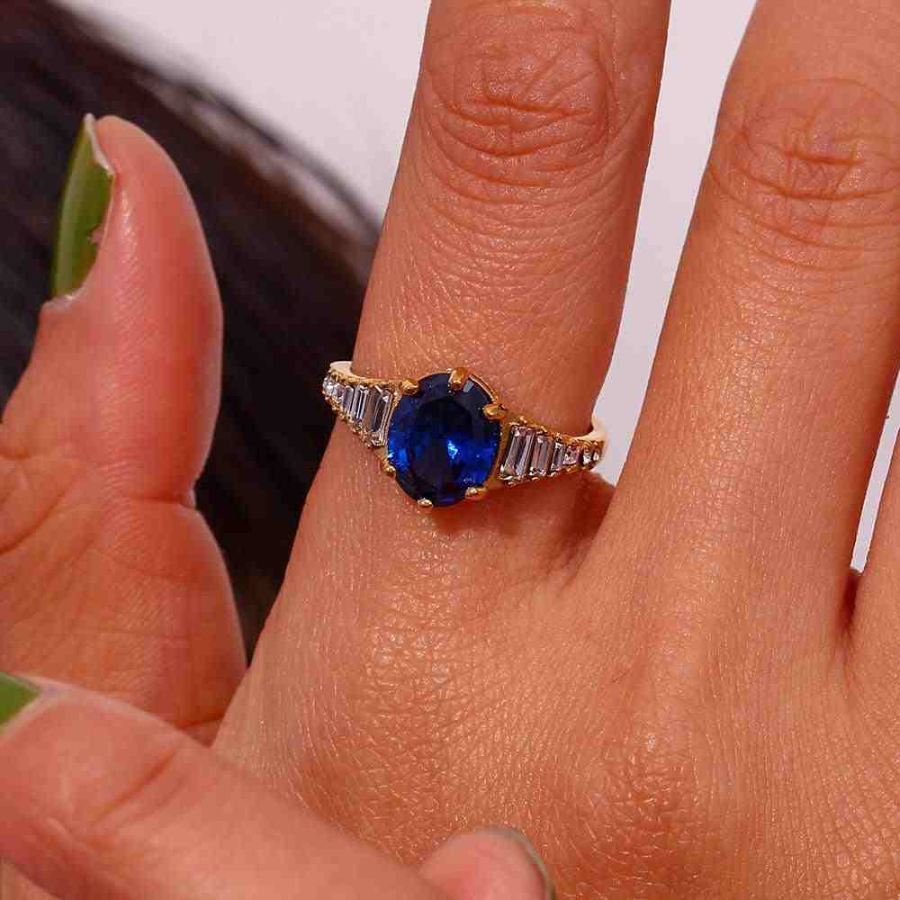Closeup of index finger wearing zepher sapphire ring with oval cut royal blue sapphire Centerpiece and Baguette Cut Zirons in both sides of Gemstone