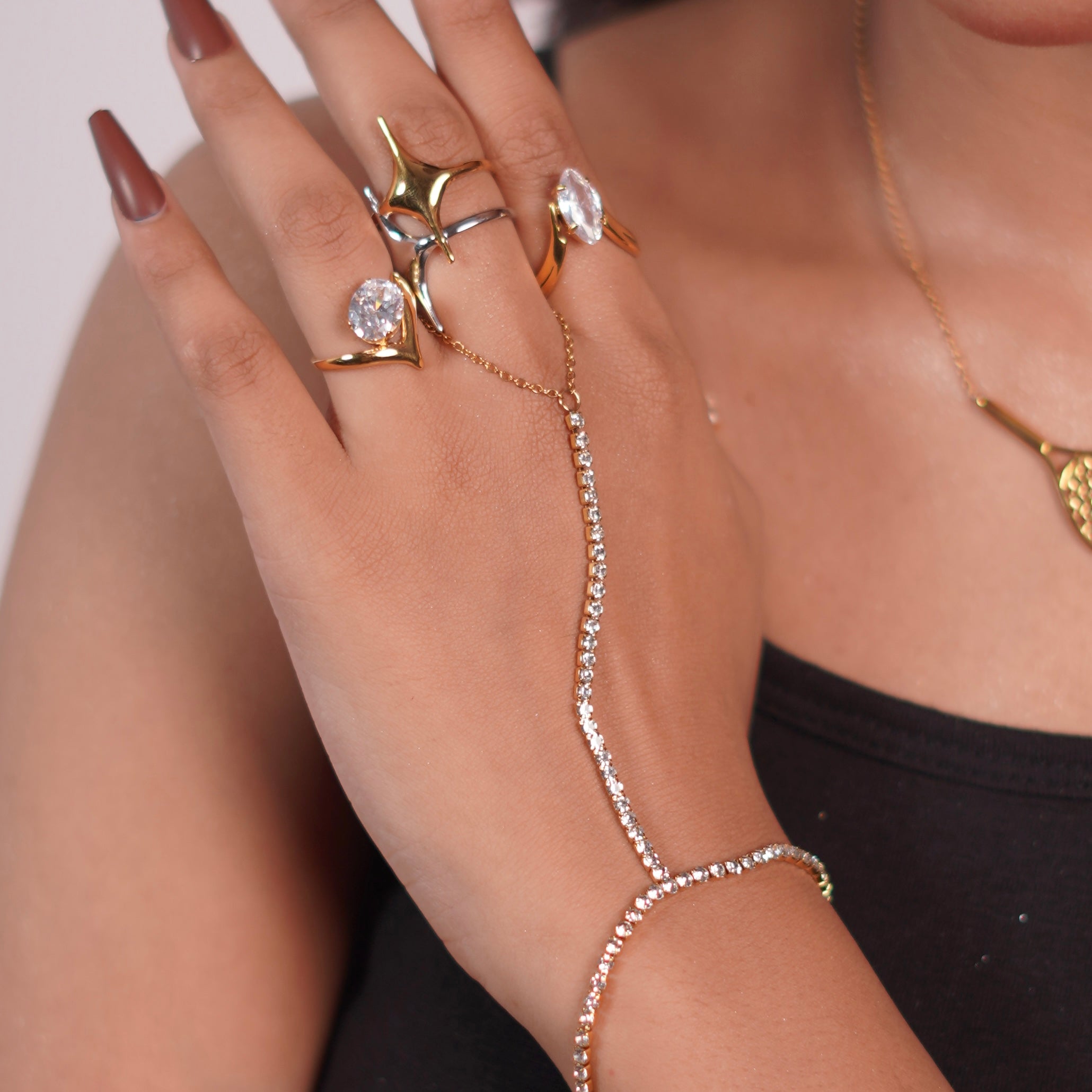 Close-up of a hand wearing gold rings and a diamond bracelet on a neutral background