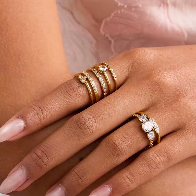 Close-up of a hand wearing multiple gold rings with gemstones on a soft pink background