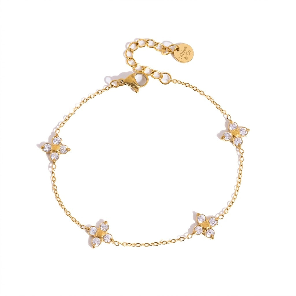 A delicate gold chain bracelet featuring five small flower motifs with white pearl-like centers and clear rhinestone petals, displayed on a clean white background.