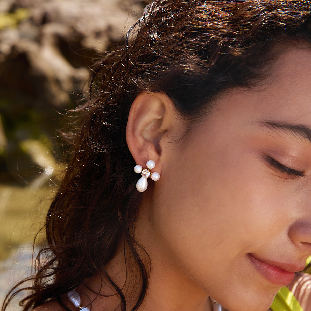 Maison Noir Collection - Close-up of a woman wearing pearl earrings with a blurred natural background