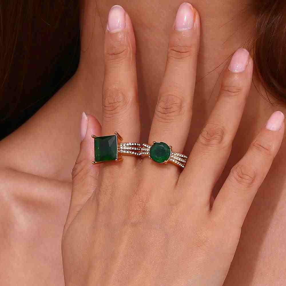 Girl wearing 18k gold plated aura ring with square emerald green stone and aurora emerald ring with round emerald stone in separate fingers.
