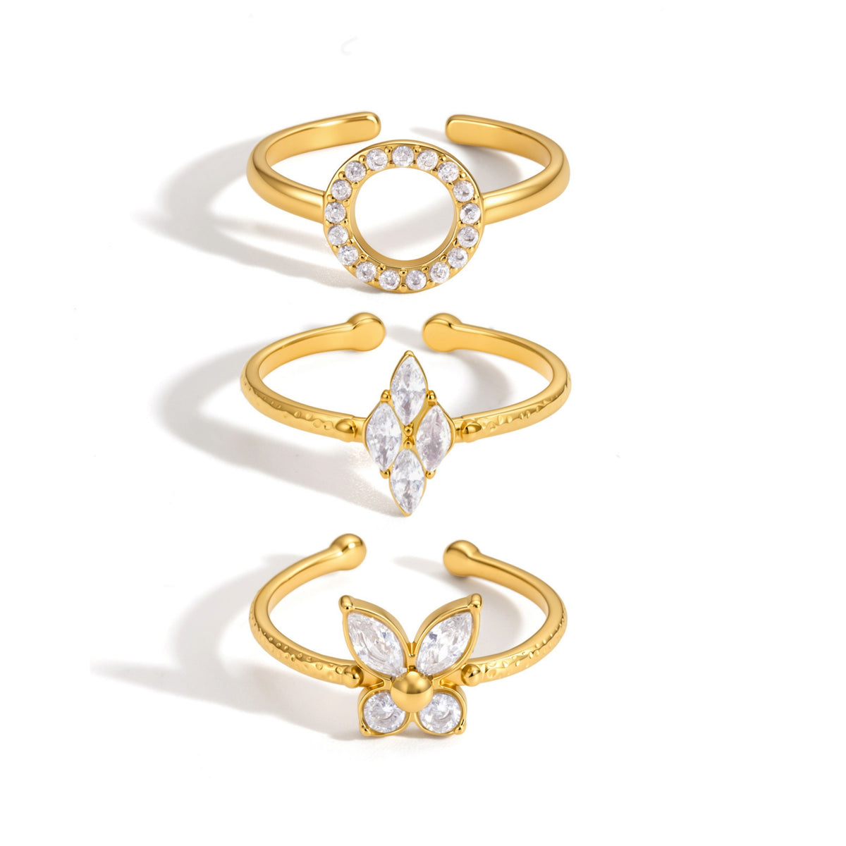 Bloom Stack Rings Set Three gold open ring earrings with clear crystal embellishments, arranged vertically on a white background. The top ring features a circular crystal halo, the middle ring has a marquise crystal cluster, and the bottom ring is shaped like a butterfly with crystal wings.