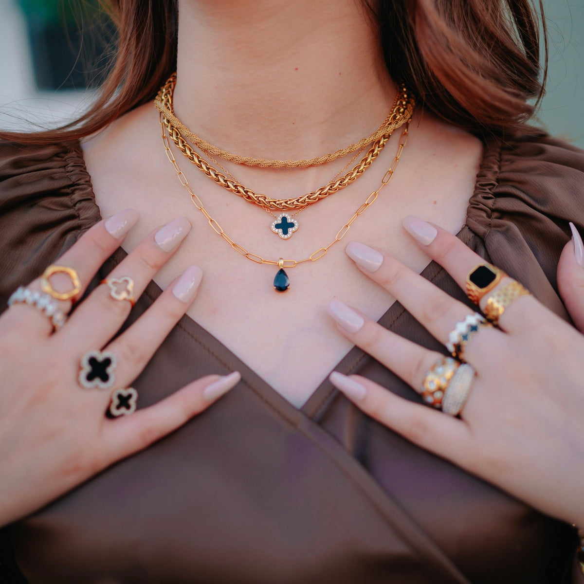 Closeup of woman wearing Harper twisted-rope jean pendant, Midnight Clover, and Greek woven necklaces stacked together with Clover Black, Clover White, Malachite Black mesh rings, Nysera ring, and studded Domsley ring midnight clover ring, fifi ring, hollow clover ring and noval ring