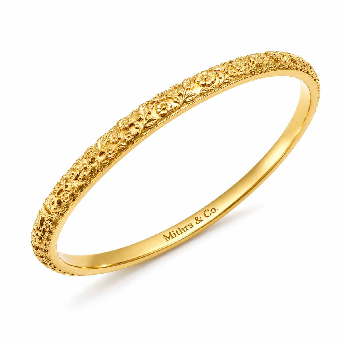 A gold heritage bangle bracelet with an intricate floral filigree pattern on the outer band and 'Mithra & Co.' engraved on the inner band, shown on a clean white background.