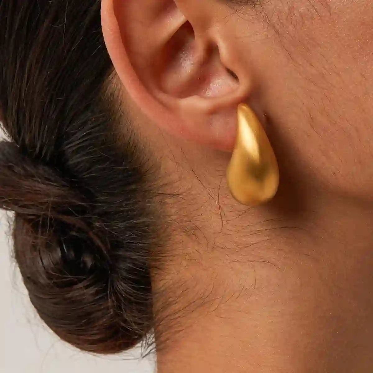 Closeup of a GIrl's right ear wearing 18k Gold Plated Brushed Matte Teardrop Contour Earrings - Hotte Matte.