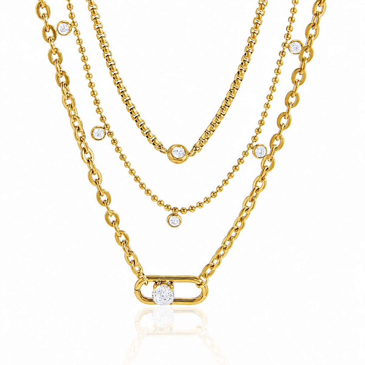 A layered gold necklace set featuring three distinct chain styles: a curb chain with a large oval link and a single bezel-set clear stone, a box chain with a small round bezel stone, and a delicate beaded chain with a small bezel stone, all displayed on a clean white background with a subtle reflection.