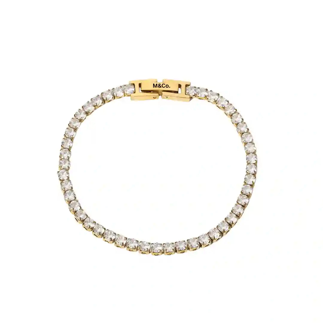 Studio shot of 18k Gold Plated Verity tennis bracelet with clear crystals and an "M & Co." engraved with black ink gold clasp.