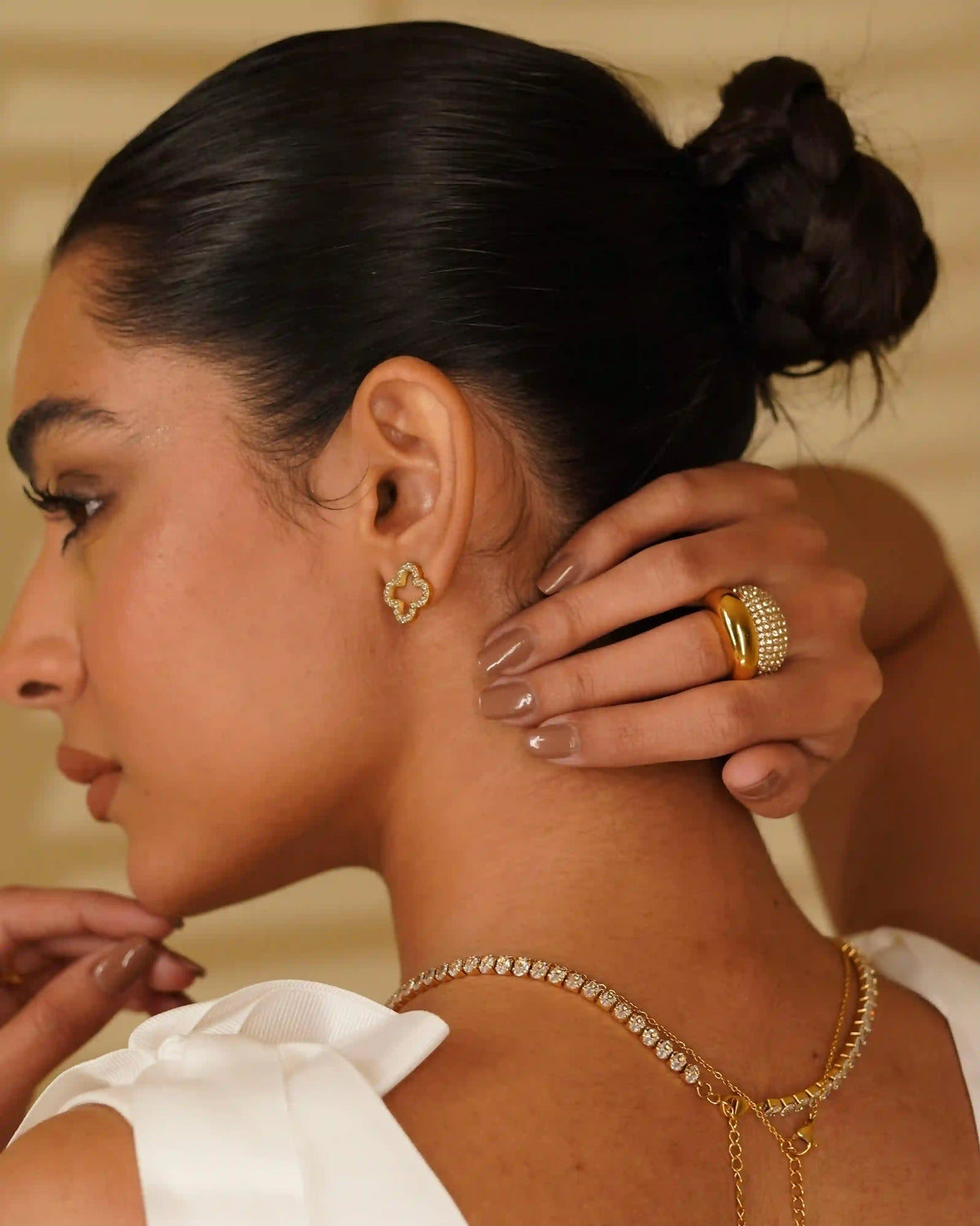 Back View Closeup of a woman wearing hollow clover studded studs and necklace with linea necklace and studded domsley and domsley rings stacked in middle finger.