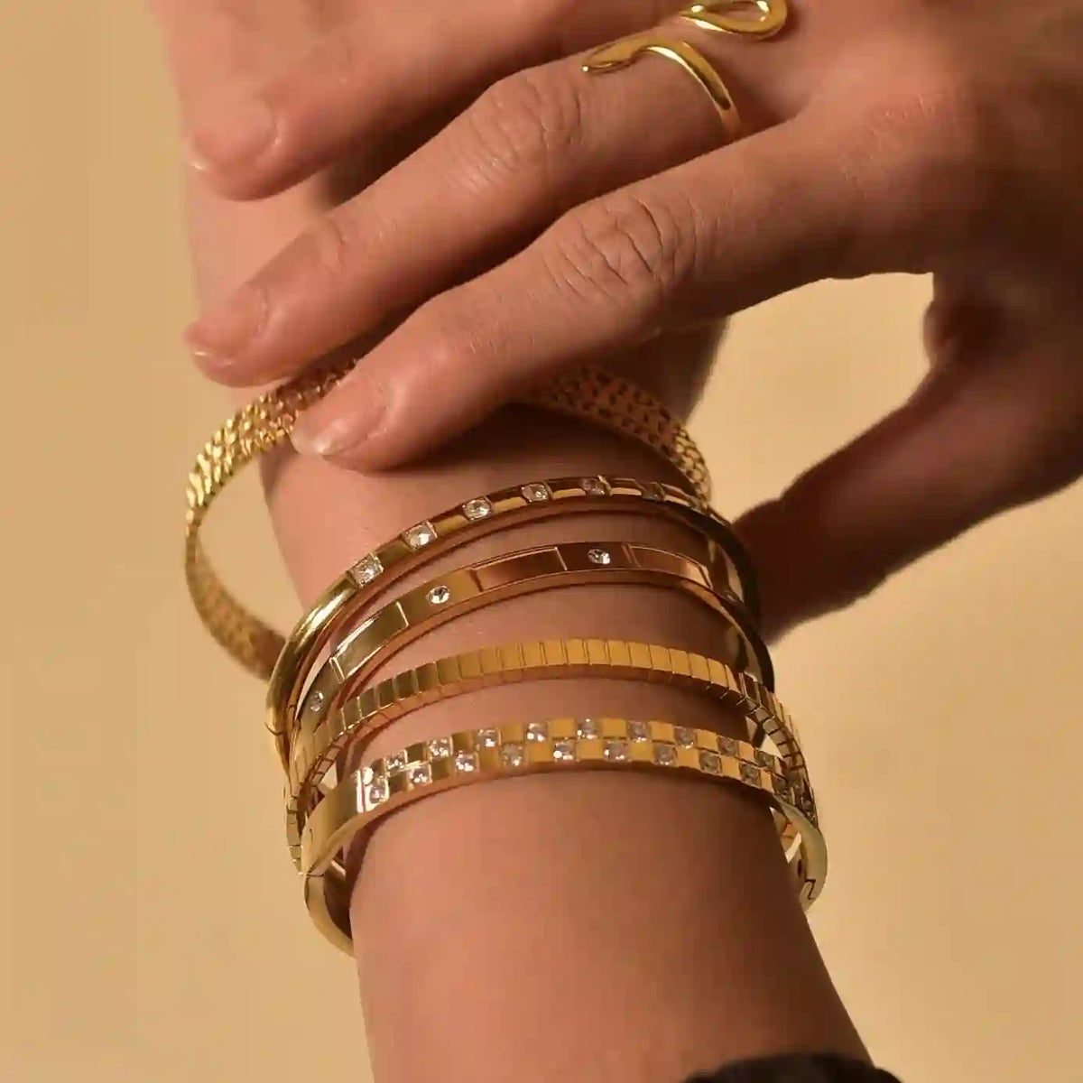 Closeup of a woman's hand wearing 5 stacked bangles including gold hinged bentley cuff bangle claro cuff bangle and 3 others.
