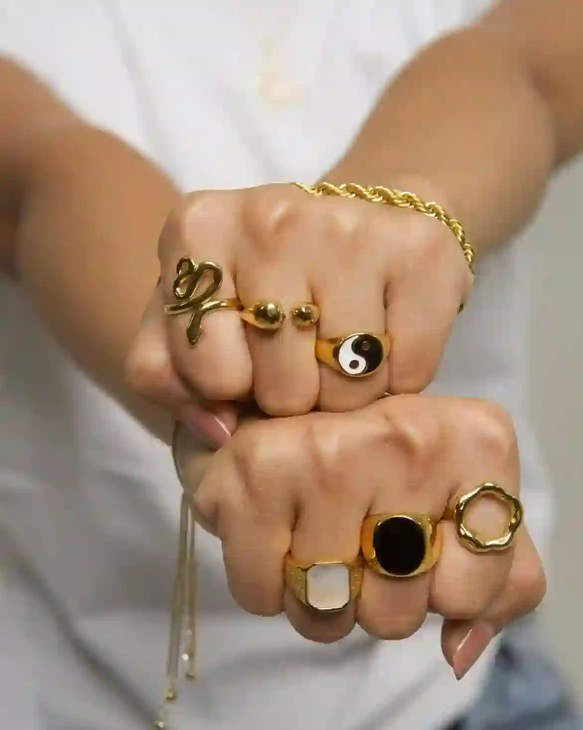 Both hands wearing gold-plated rings on 3 fingers including ramsey signet yin yan and other rings and gold bracelets, styled over casual white t shirt.