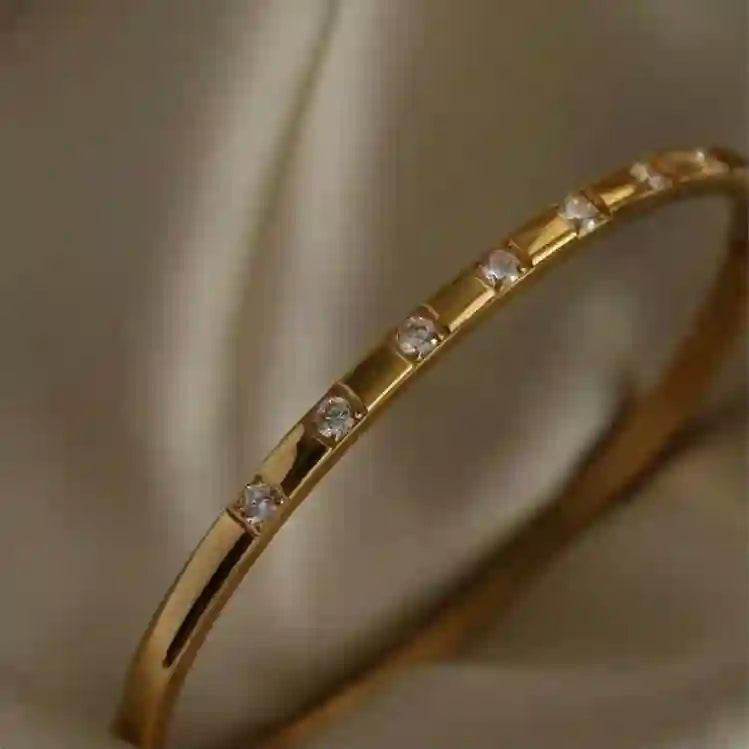 Claro Cuff 18k Gold Plated bangle with small round cut zircons a beige background