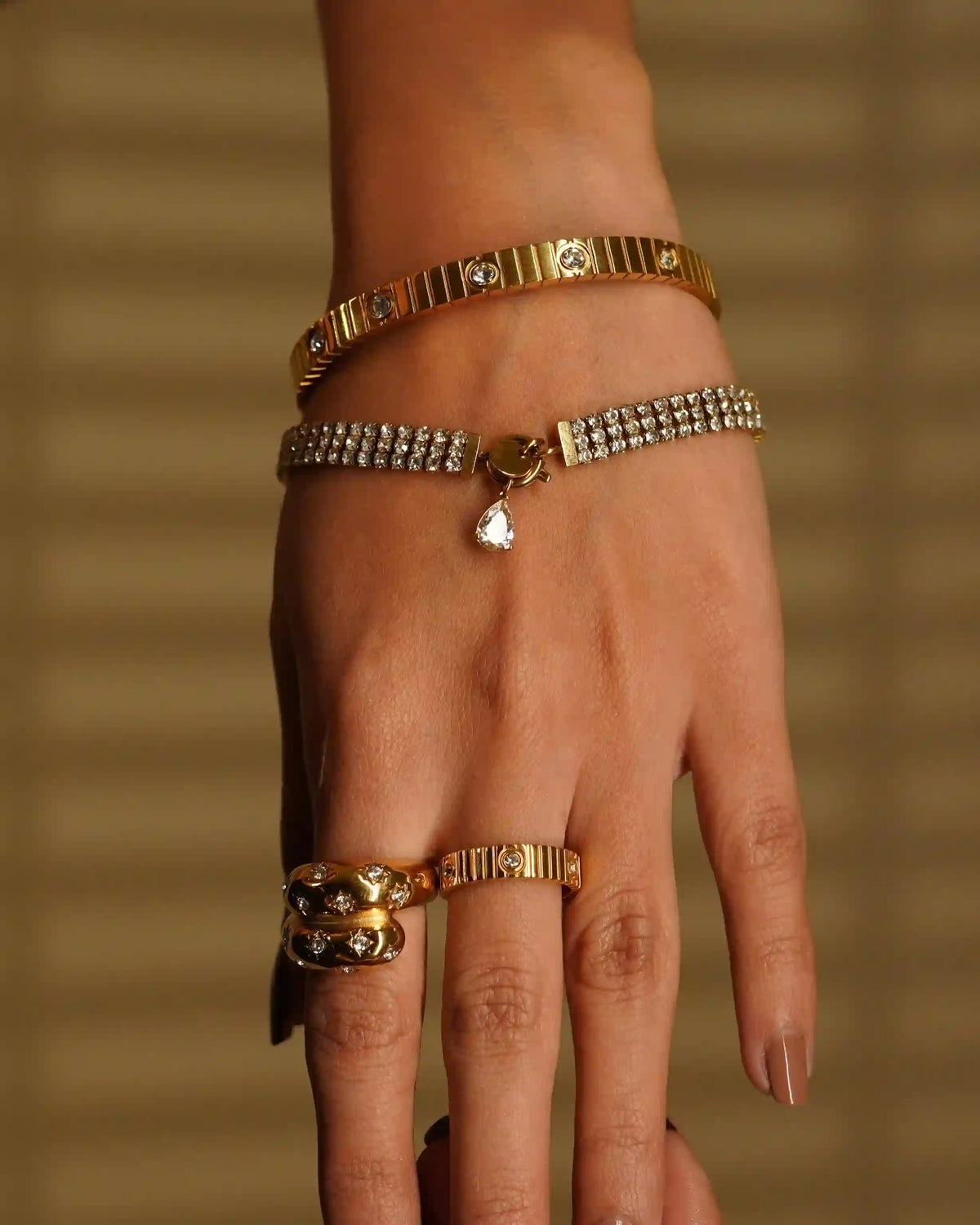 closeup of a woman's wrist wearing kendall diamontee bracelet, coil studded bangle and coil studded ring in middle finger and celestial ring in index finger.