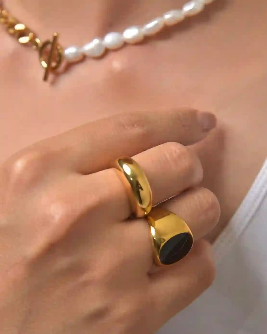 Detailed macro shot focusing on a hand wearing the 18k gold plated Domsley wedding band ring with a black stone ring and matching gold-plated necklace for a cohesive statement look.