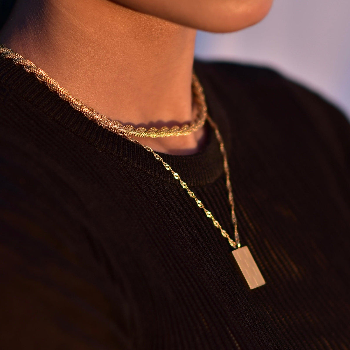 Closeup of girl wearing 18k Gold Plated Harper twisted rope chain necklace with another neck chain on a black shirt.