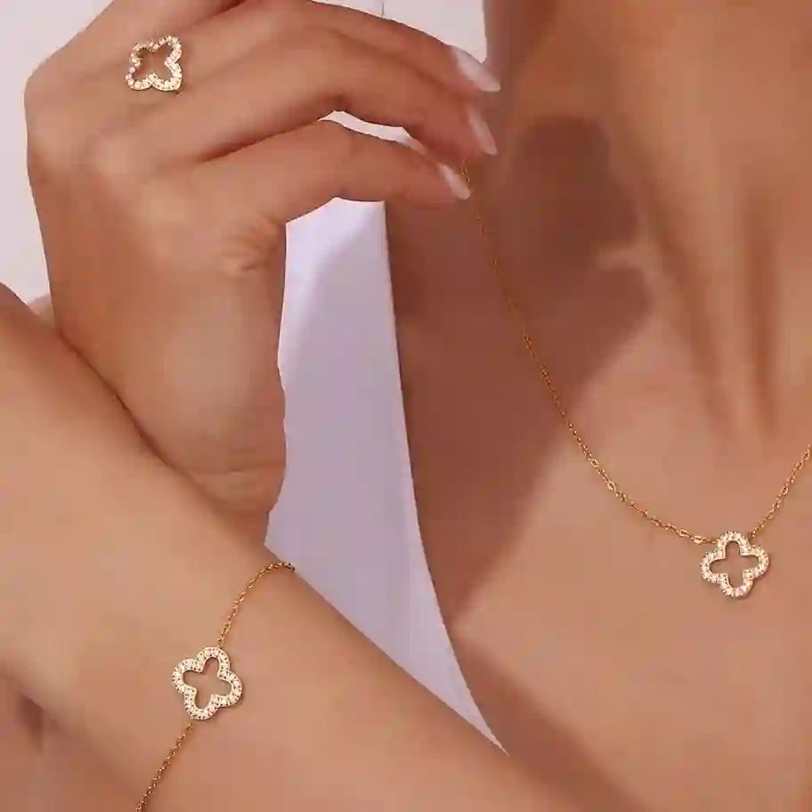 Closeup of a model wearing hollow clover studded ring, necklace and bracelet all with an open-work 4 leaf clover floral motif.