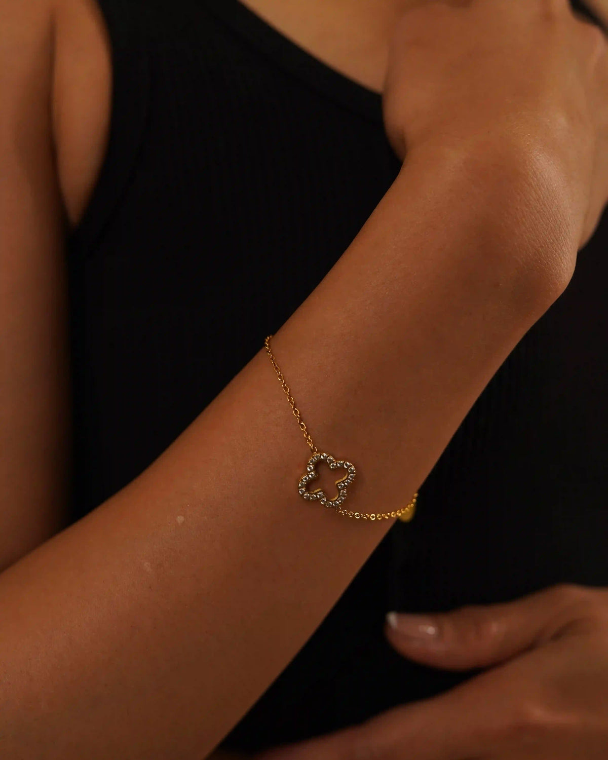 Closeup of a hand wearing Hollow Clover Studded Bracelet with Pave ZIrco Layering. an 18k gold plated Hand chain with Open-Silhouette Quatrefoil Design.