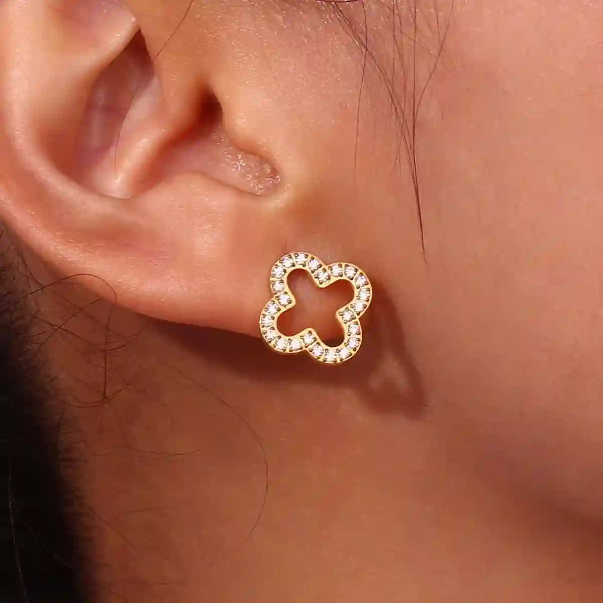 Closeup of a woman's right ear wearing hollow clover studded studs.