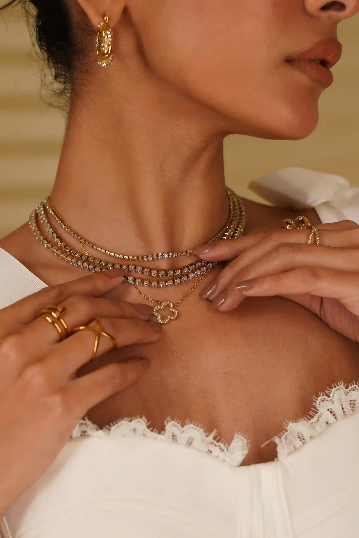 Closeup of a woman wearing Linea Necklace and Hollow Clover Studded necklace and gold plated rings and  earrings.