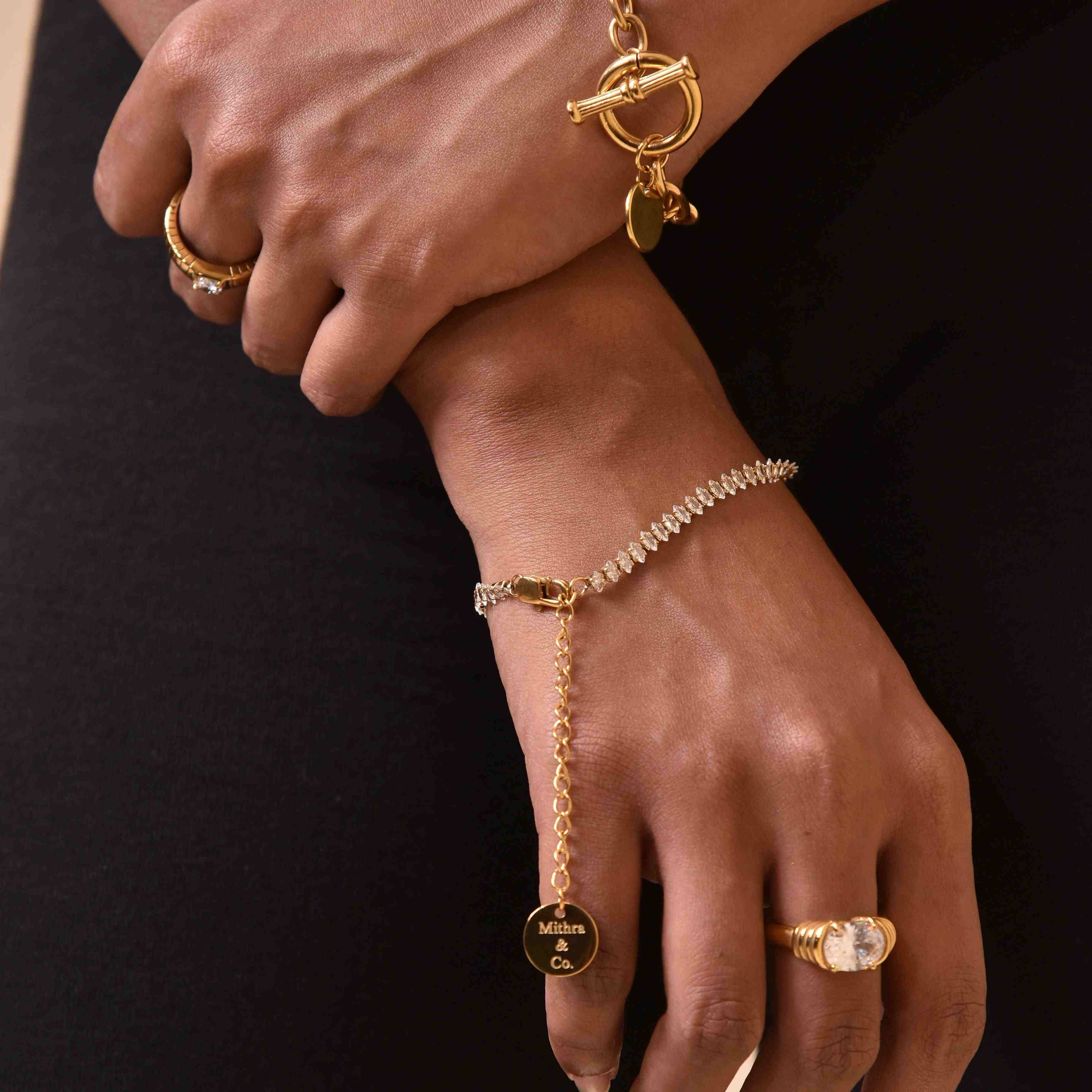 Woman wearing 18k Gold Plated clasp bracelet with clear stones and gold rings on dark background