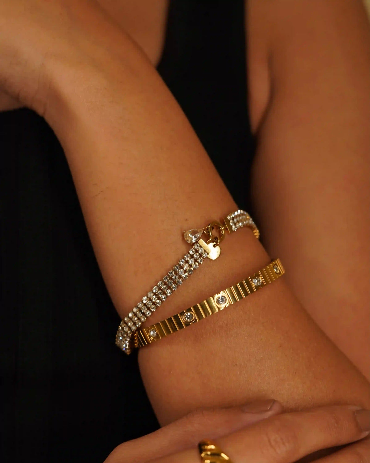 Closeup of a woman's hand wearing Kendall Diamontee Bracelet and coil studded bangle. 18k Gold Plated Wristwear.