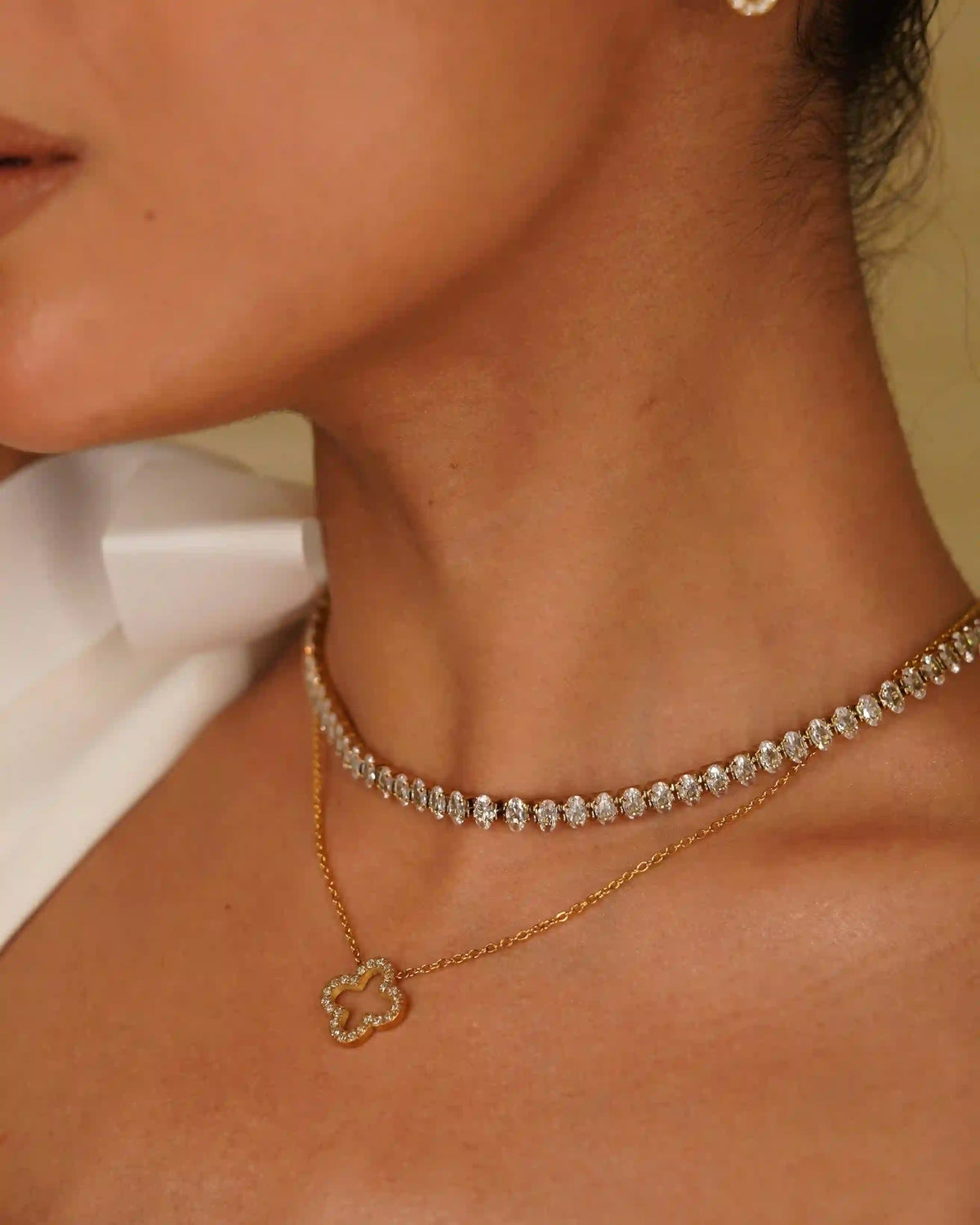 Closeup of a girl wearing Hollow clover studded necklace layered with linea tennis necklace featuring beads style faceted CZ box chain links.